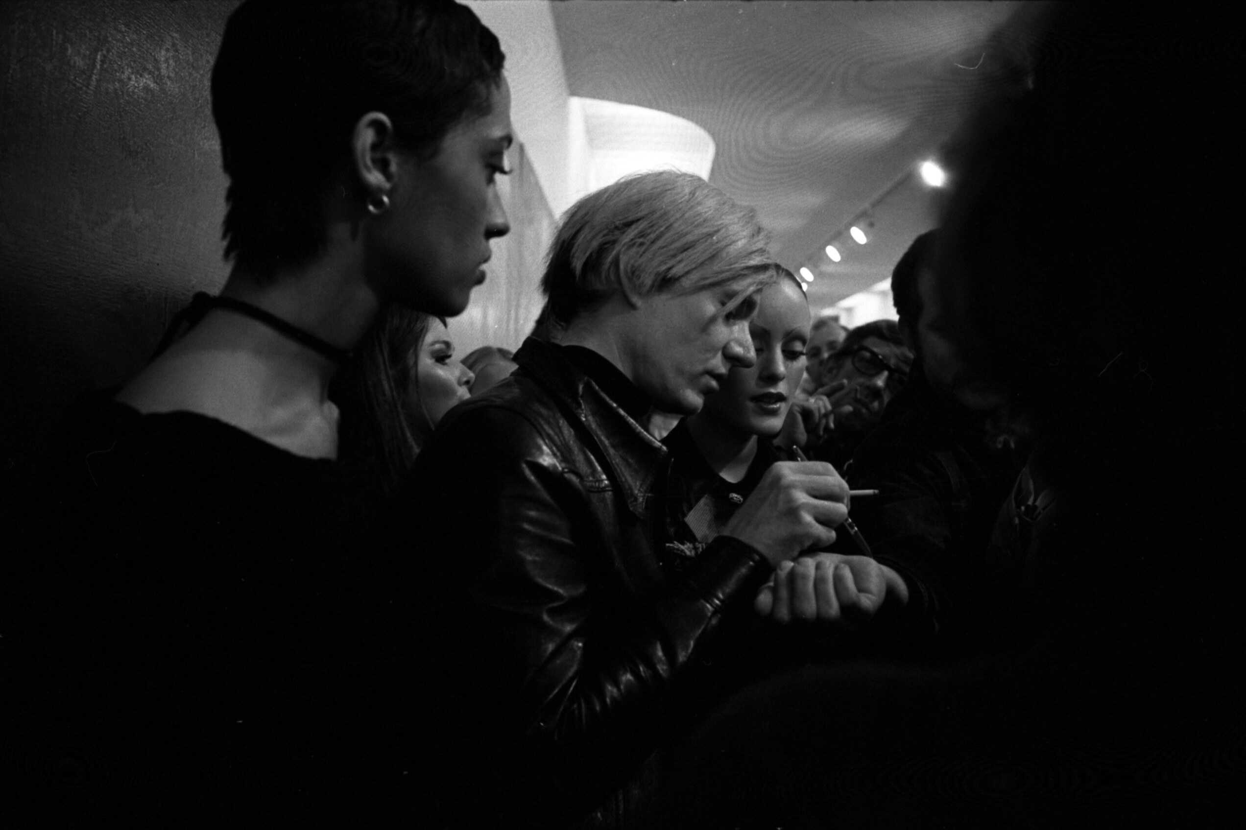 Andy Warhol beugt sich über einen Tisch und signiert 1970 im Pasadena Art Museum Autogramme.