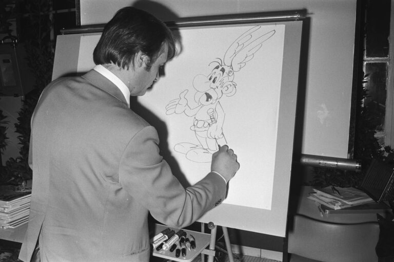 Albert Uderzo sitzt an einem Tisch und zeichnet bei einem Auftritt in Amsterdam 1971 Asterix.